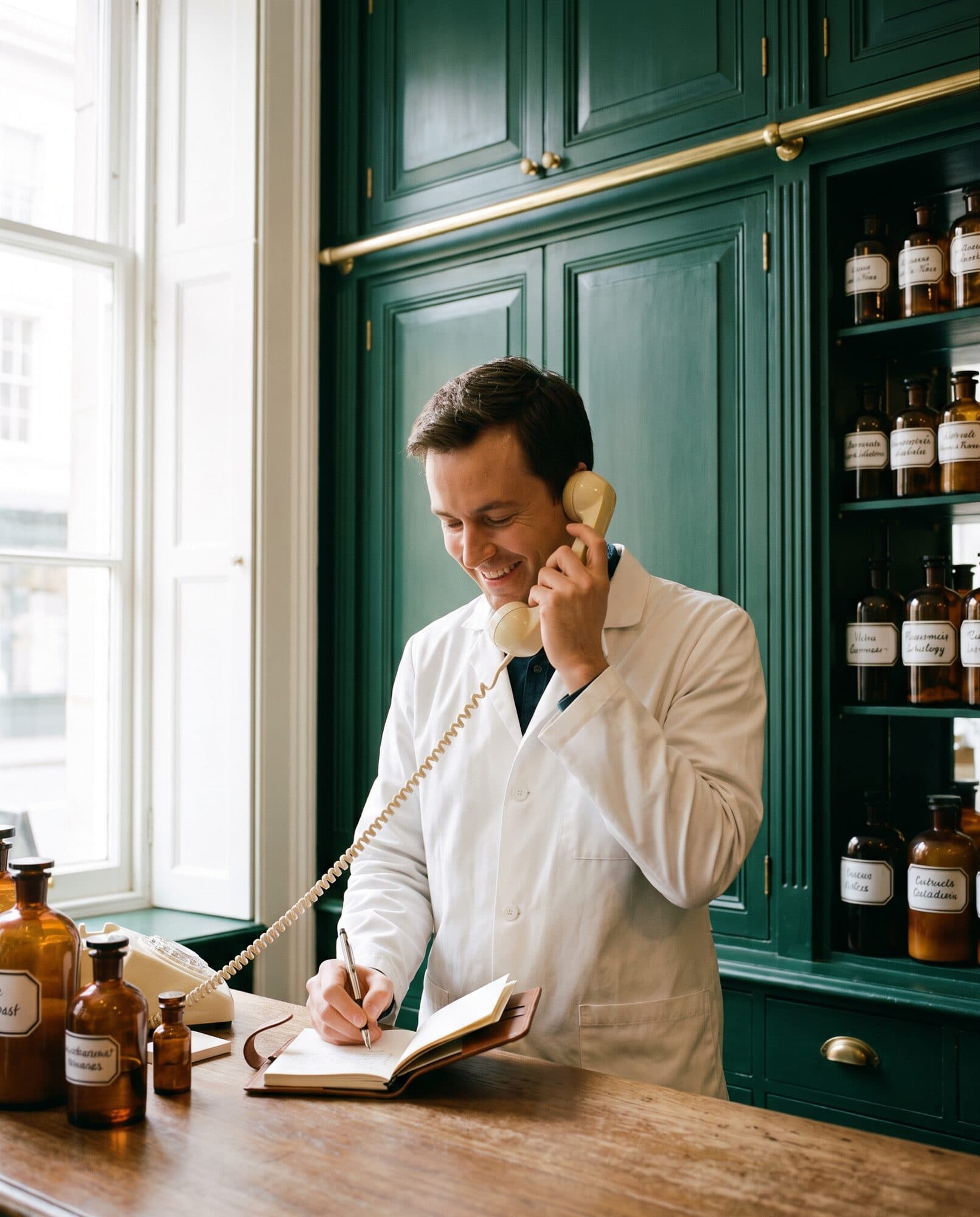 A pharmacist taking a call at the back counter and writing in a notebook